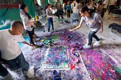 several young people gather around a canvas splattered with purple paint for a group painting project