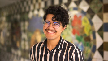 man with dark curly hair smiling in front of a mosaic wall