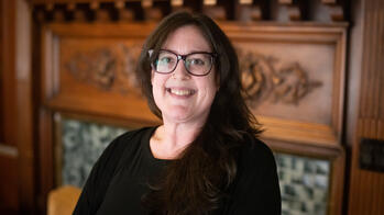 photo of a person smiling in a black shirt in front of a fireplace