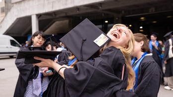 two students hugging, one with their face visible is smiling. both are in commencement regalia
