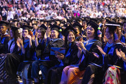 several graduating students seated in regalia among a large crowd at Commencement ceremony