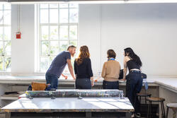 faculty member talking to four students at a desk