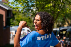Student smiling at the camera over their shoulder, pointing to "staff" on the back of their tee shirt