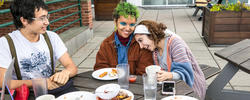 three students laugh together while eating at an outdoor patio table