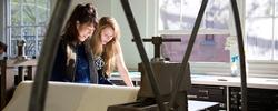 Two people are working in Benson Hall on a printmaking machine