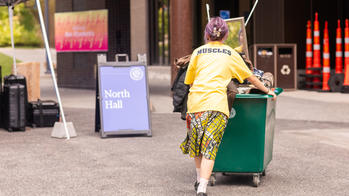 a student pushes a large storage bin toward a residence hall entryway
