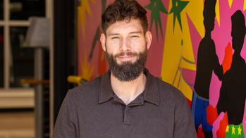 A man with a beard smiling in front of a mural