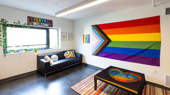 photo of the pride room, a room with a large pride flag, black couch, and rainbow pillows