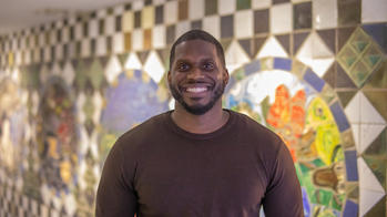 photo of a man smiling infront of a mozaic wall