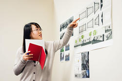 a student points to prints on a wall featuring digital renderings of architectural work