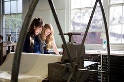 Two people are working in Benson Hall on a printmaking machine