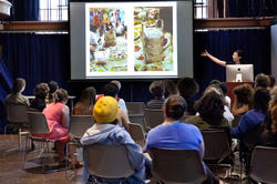 A group of RISD graduate students attend an info session where the speaker is presenting information to the group on a projector.