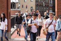 RISD students walk on red brick bridge, moving away from an office building