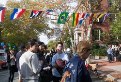 students and guests gather at outdoor event with collection of national flags hanging overhead