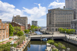 buildings flank a canal running through downtown Providence with blue sky and white clouds visible in the background