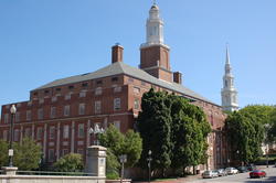 a brick building with several white steeples with green trees at the building's front and blue sky in the background