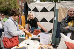 Two people are working a booth with fabric art pieces, a visitor to the booth is holding a yellow fabric piece.